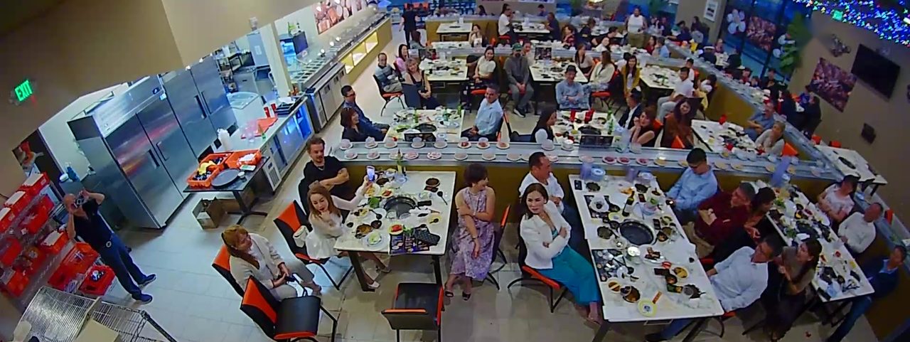A full dining room seen from above: guests at hot pot and BBQ tables, the conveyor belt running between them